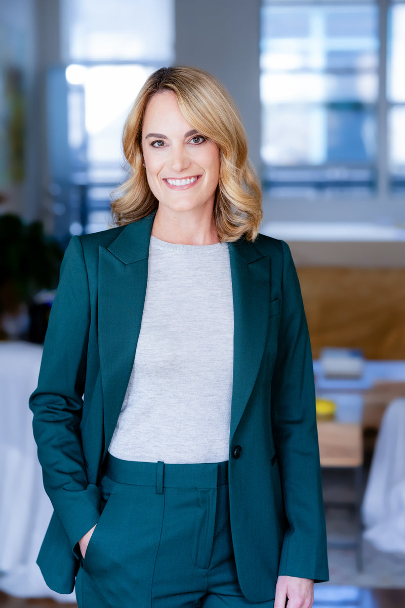 Smiling woman in a green suit standing in a bright, modern interior.