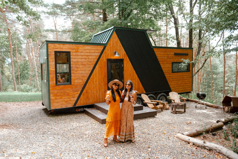 Two women pose in front of a modern cabin in a forest.