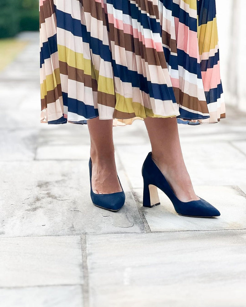 Woman wearing a colorful pleated dress and navy high heels.