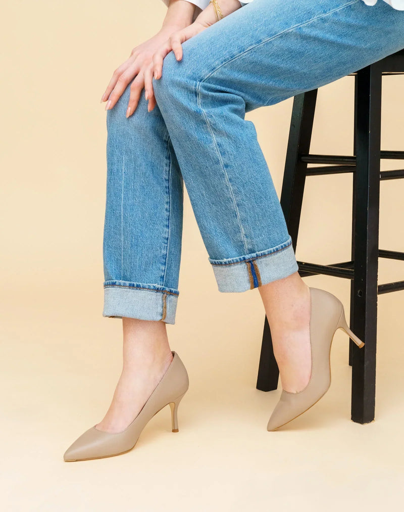 Woman wearing beige pointed-toe ALLY Shoes pumps with cuffed blue jeans while seated on a black stool.