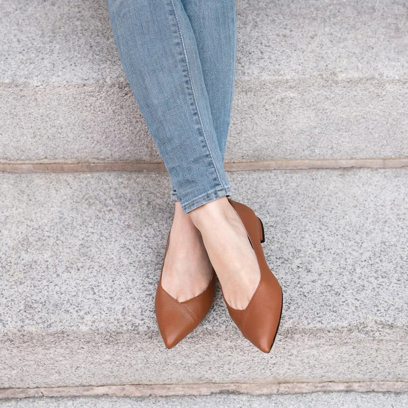 Woman wearing caramel leather pointed-toe ALLY Shoes flats with light-wash jeans on stone steps.