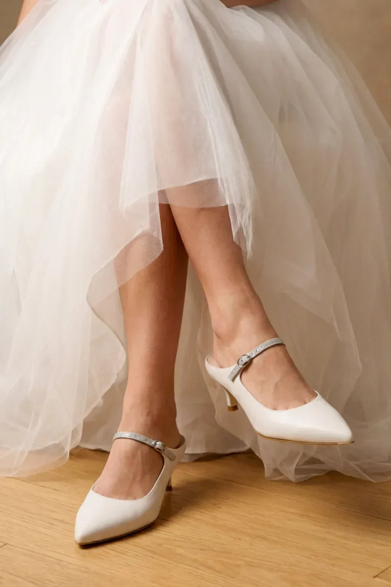 Bride wearing white pointed-toe ALLY Shoes with sparkling straps and kitten heels under a flowing tulle wedding dress.