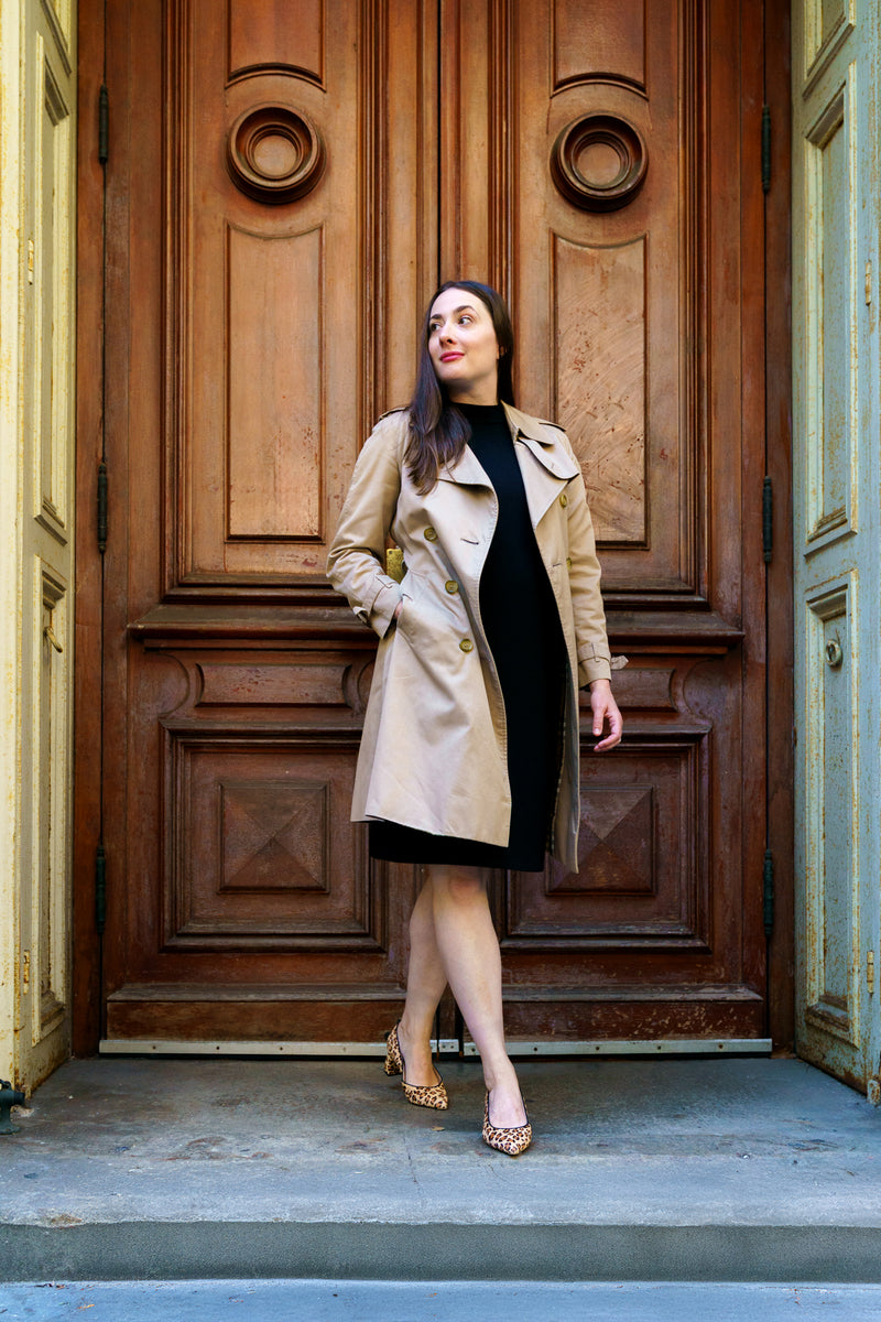 Woman in a trench coat standing in front of a large wooden door